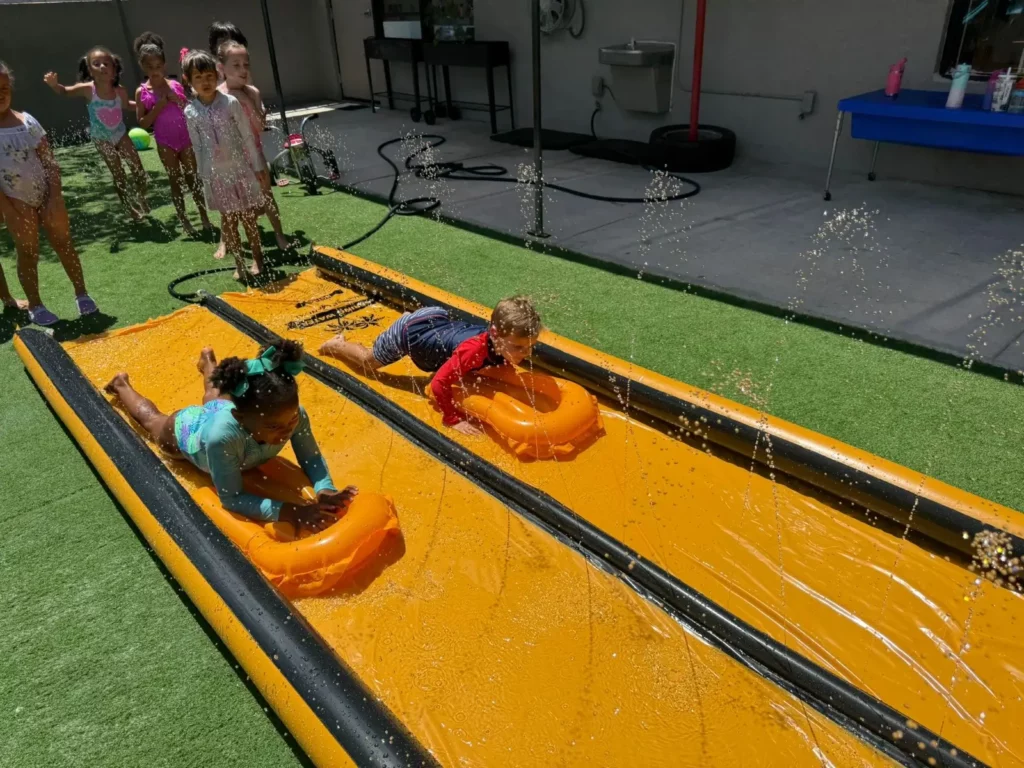 hildren enjoying a slip n slide water activity during summer camp at Pines West Academy