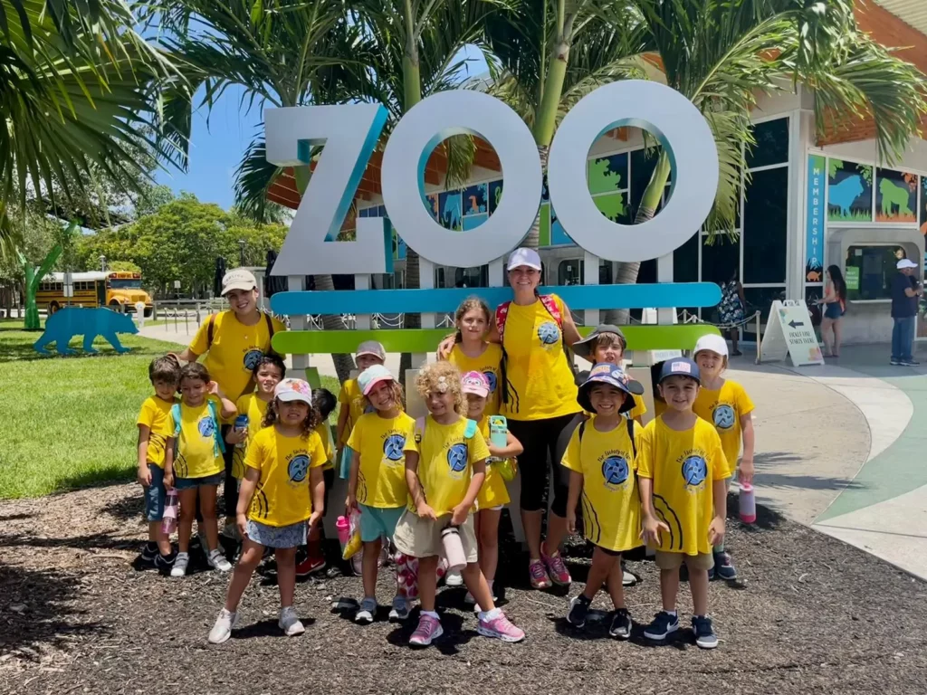 Students and teacher on a field trip standing in front of the zoo sign at Pines West Academy
