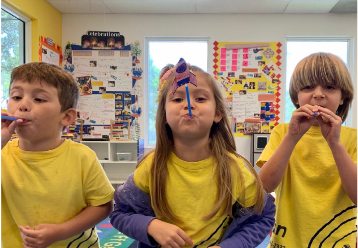 Children at Pines West Academy using oral motor skills to blow toy rockets during a science activity